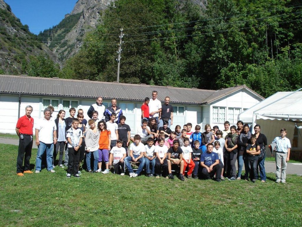 Stage FTK Olivone 2010: gruppo numeroso in gi posa davanti all'alloggio, tra montagne e prato verde